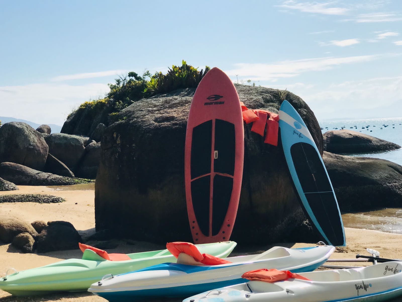 A beach with kayaks and a surfboard leaning against a rock.