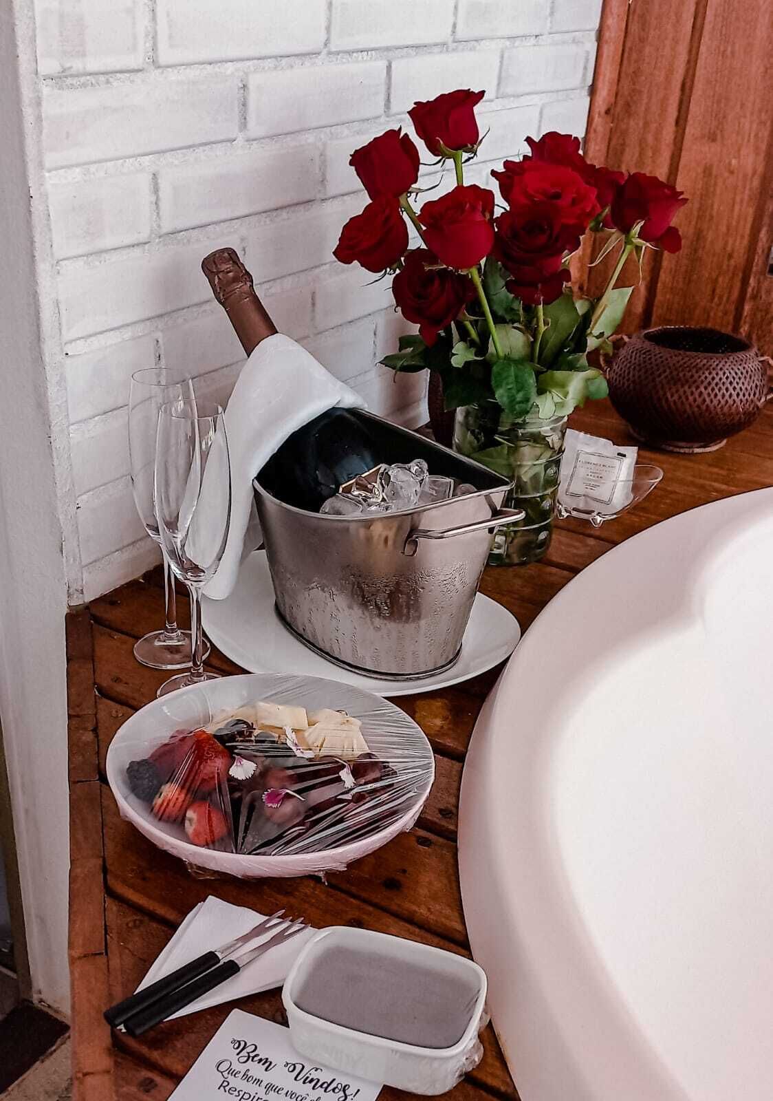 A dining table with a metal bucket, a plate of food, a vase of red roses, and a wine glass.
