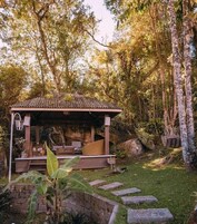 Um gazebo de madeira com telhado de azulejos, cercado por vegetação exuberante e árvores.