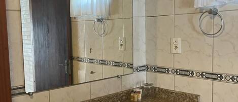 Une salle de bain avec un lavabo doté d’un plan de travail en granit, un miroir, un porte-serviettes et un porte-rouleau de papier toilette.