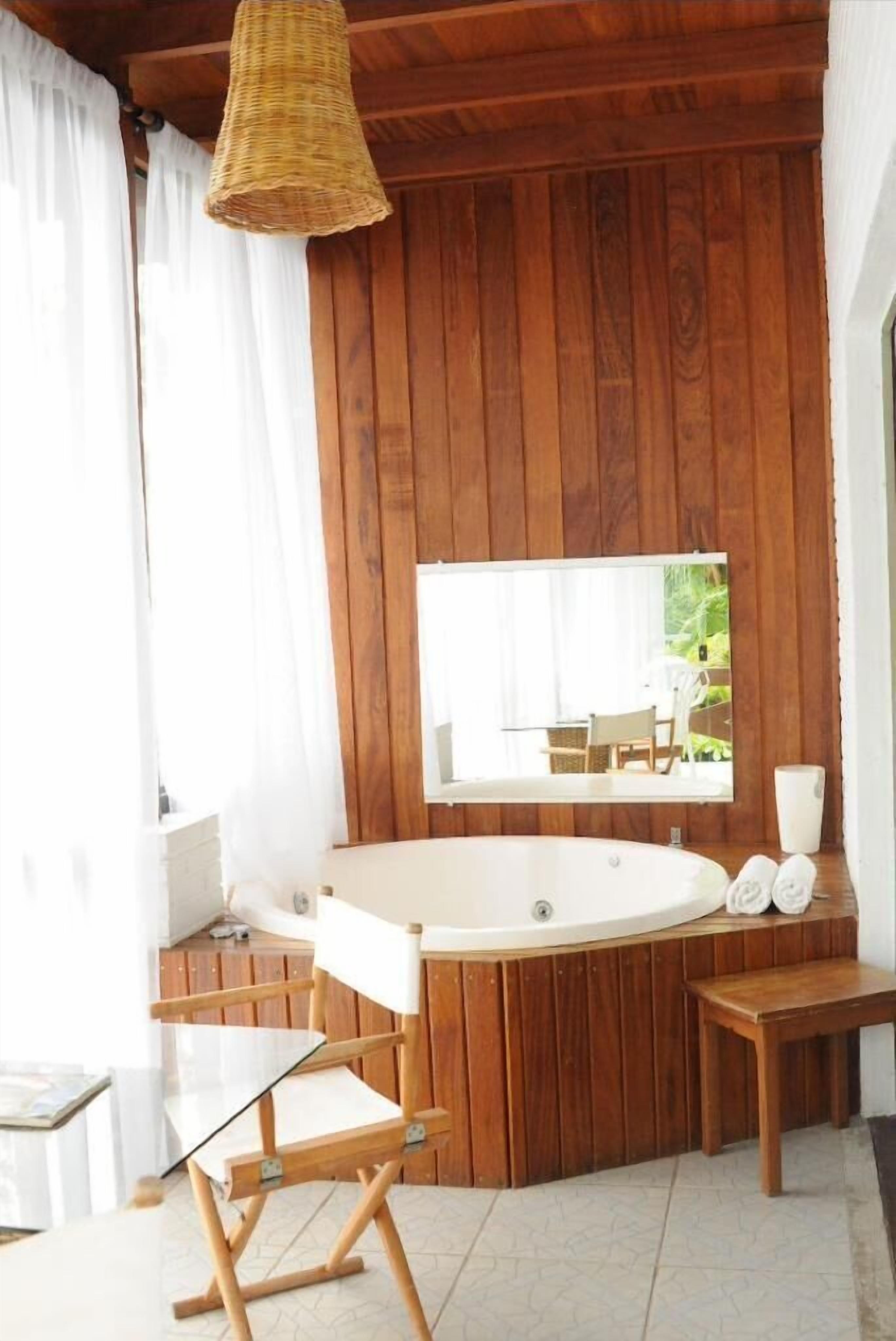 Un baño con paneles de madera, una bañera independiente, un espejo y una mesita con toallas.