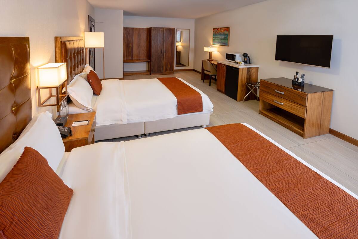 Habitació d'hotel amb dos llits, un escriptori, un televisor i un armari.