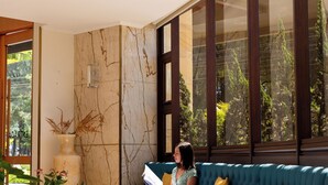 Un interior moderno con un sofá azul verdoso curvo, una pared de mármol y un ventanal con vistas a la vegetación.