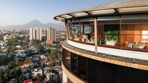 Un edificio moderno con un balcón curvo que ofrece vistas a un paisaje urbano y una montaña.