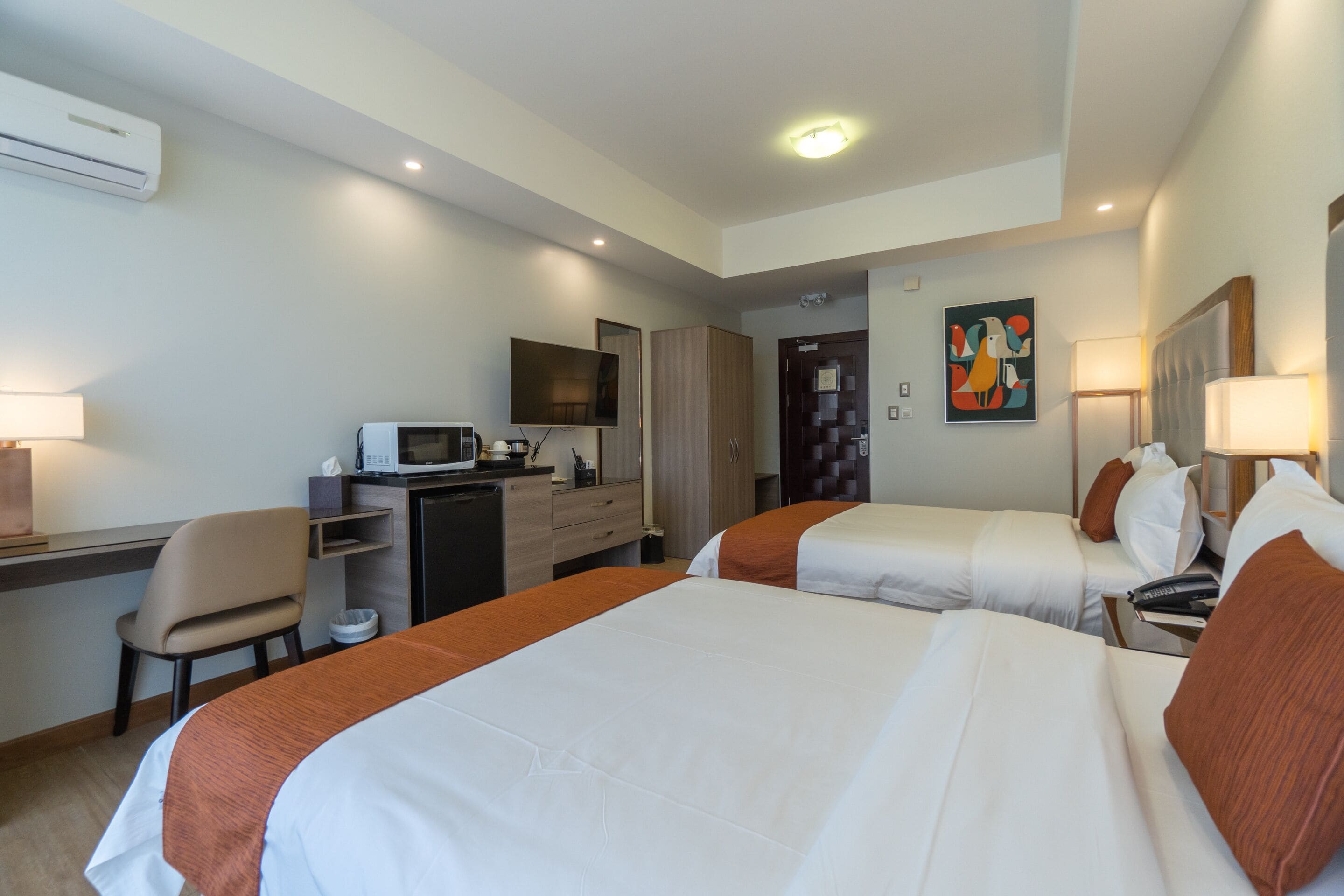 Habitación de hotel con dos camas, un escritorio, una silla, un televisor y un cuadro en la pared.