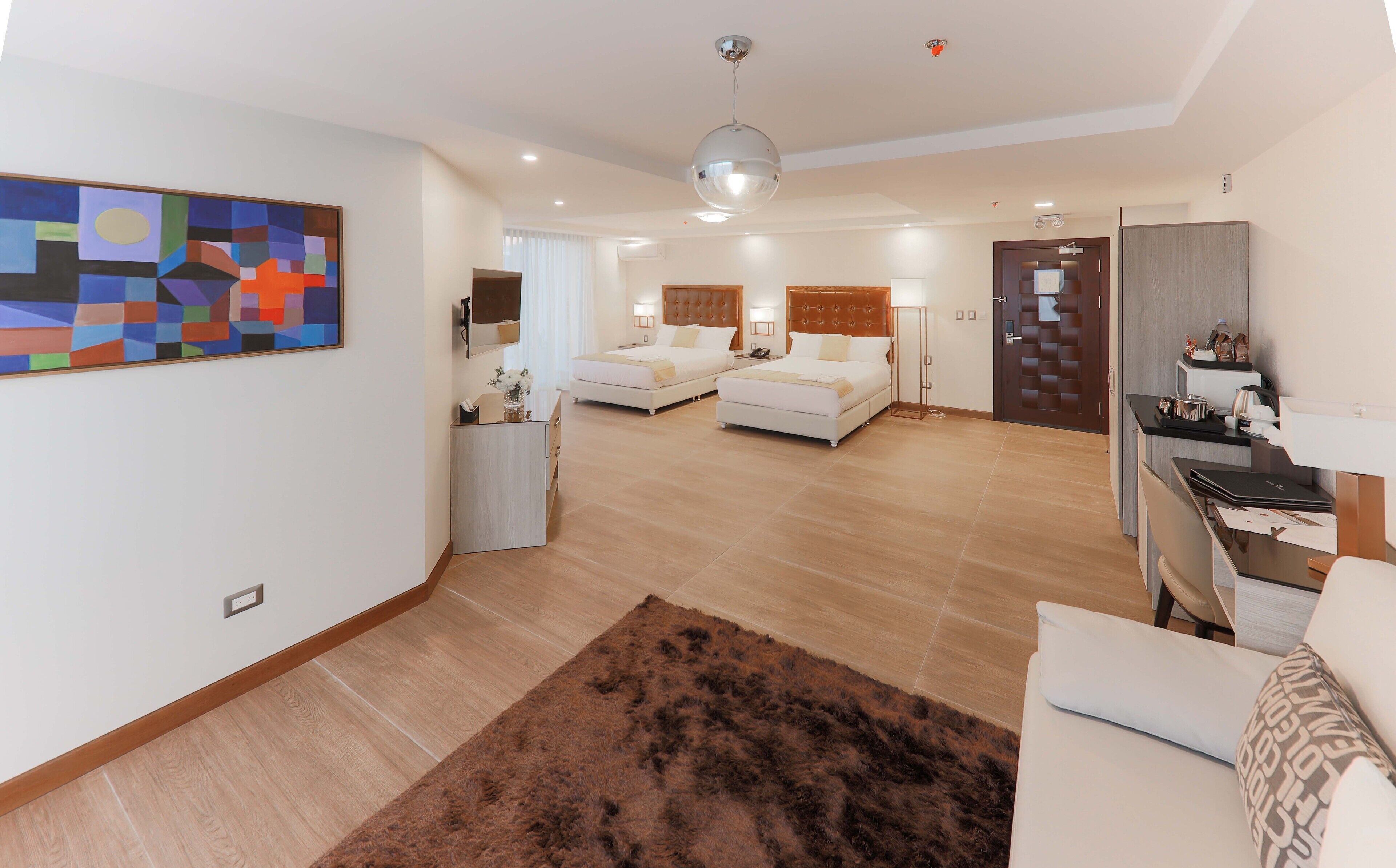 Una habitación de hotel moderna con dos camas, un escritorio, un armario y un cuadro abstracto grande en la pared.