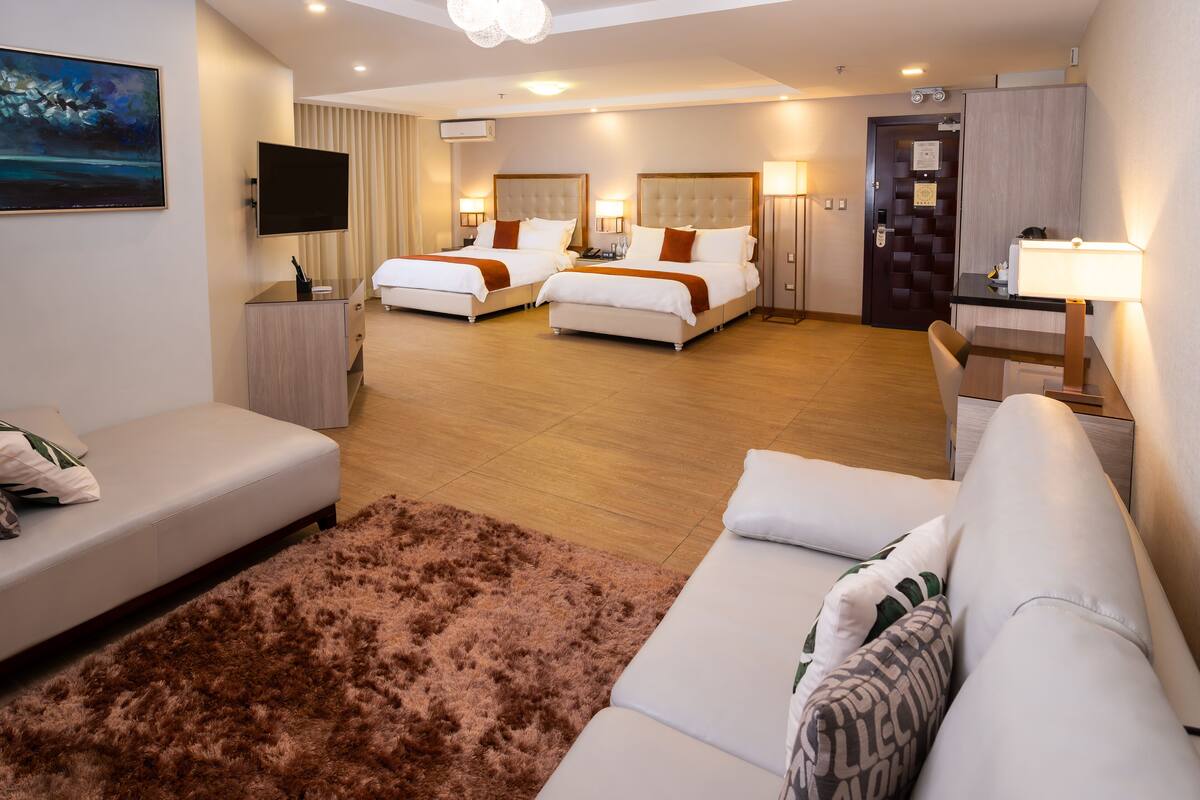 Habitació d'hotel amb dos llits, un sofà, una televisió i un escriptori amb una làmpada.