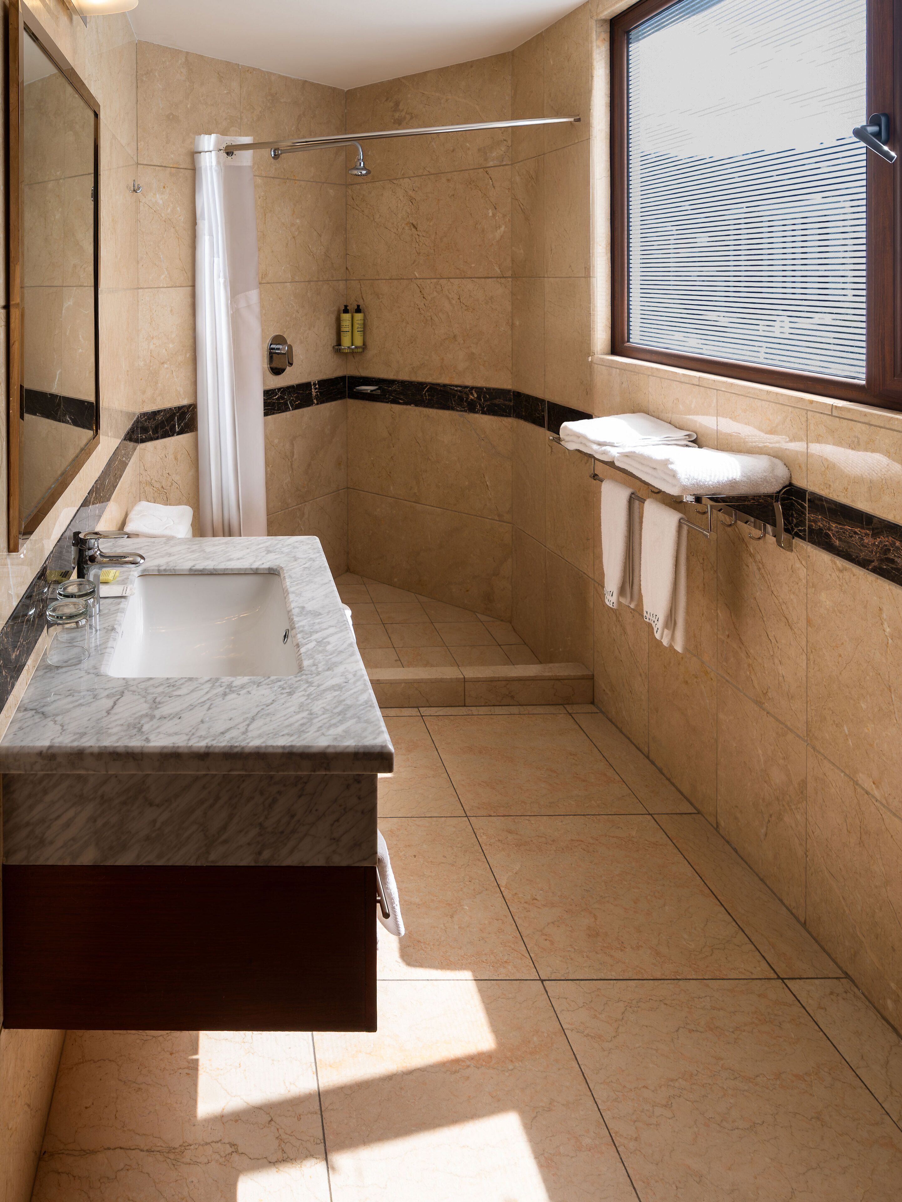 Un baño moderno con lavamanos de mármol, ducha y tocador con perchero.