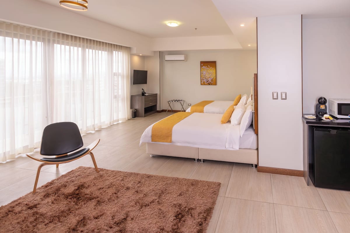Una habitació d'hotel moderna amb un llit gran, una taula de treball amb microones, televisió i un finestral gran amb cortines.