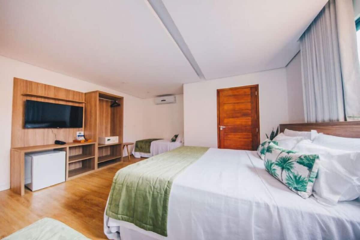 Ein Schlafzimmer mit Bett, Wandfernseher, Holzschrank, kleinem Schreibtisch und Tür.