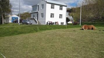A white building with a staircase leading to a deck, surrounded by a grassy area with a dog lying down.