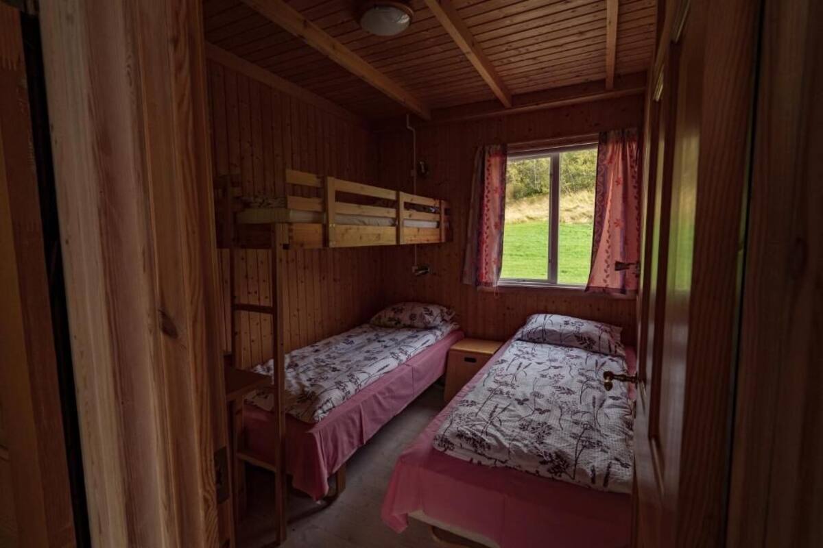 A cabin with two bunk beds, wooden walls, a window with curtains, and a small table.