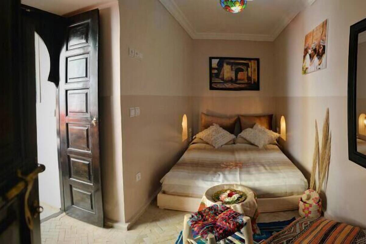 Un dormitorio con cama, mesita de noche, una silla y un espejo.