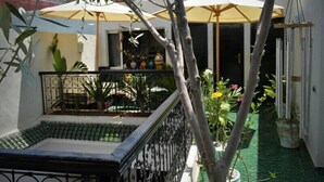 Un patio con una piscina pequeña, plantas en macetas y sombrillas al aire libre.