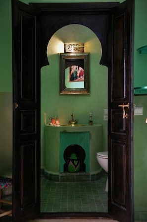 A bathroom with a green wall, a framed picture above the sink, and a toilet visible through an archway. - Riad Sardinas & Chili (Marrakech)