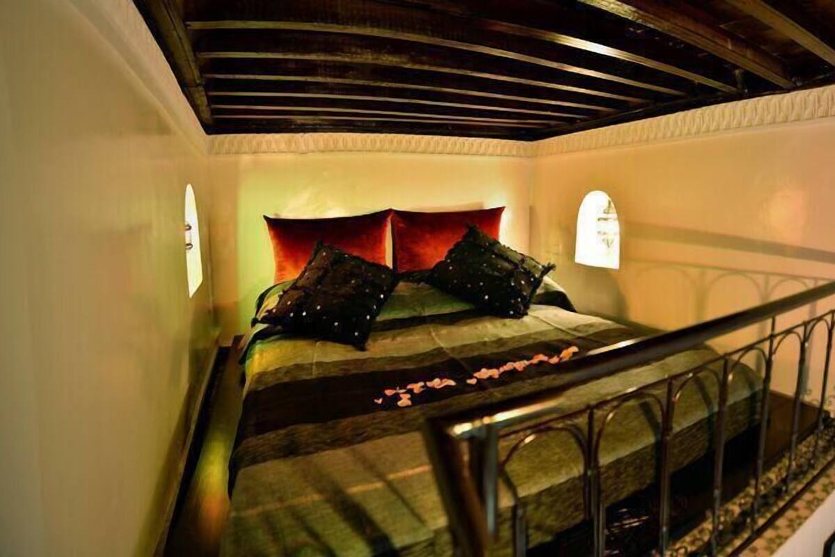 Una escalera conduce a un dormitorio con una cama, almohadas y una mesita de noche.