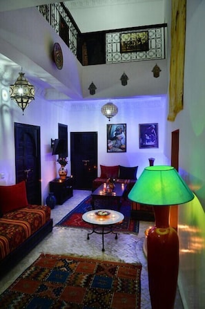 A living room with a high ceiling, a staircase, and a chandelier. There are two doors, a sofa, a table, and a lamp. - Riad Sardinas & Chili (Marrakech)