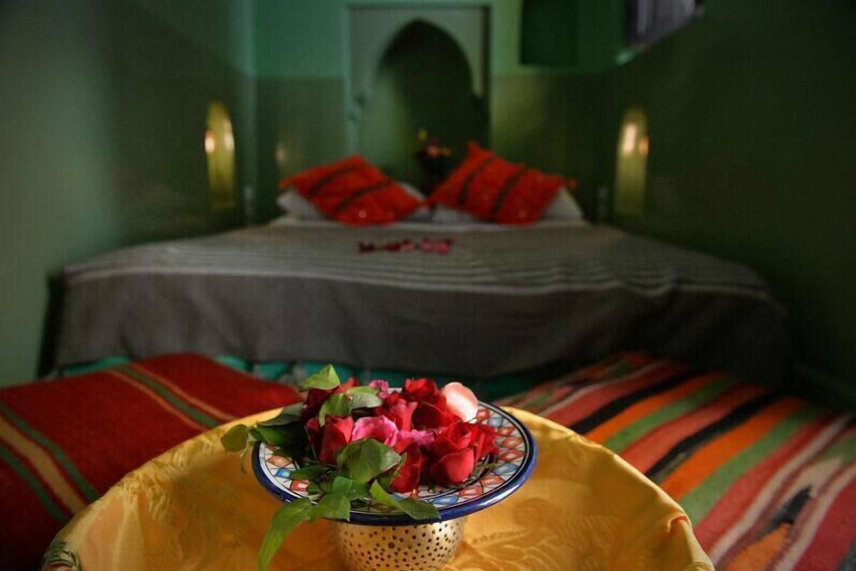 Una cama con almohadillas rojas y un cuenco de flores en primer plano.