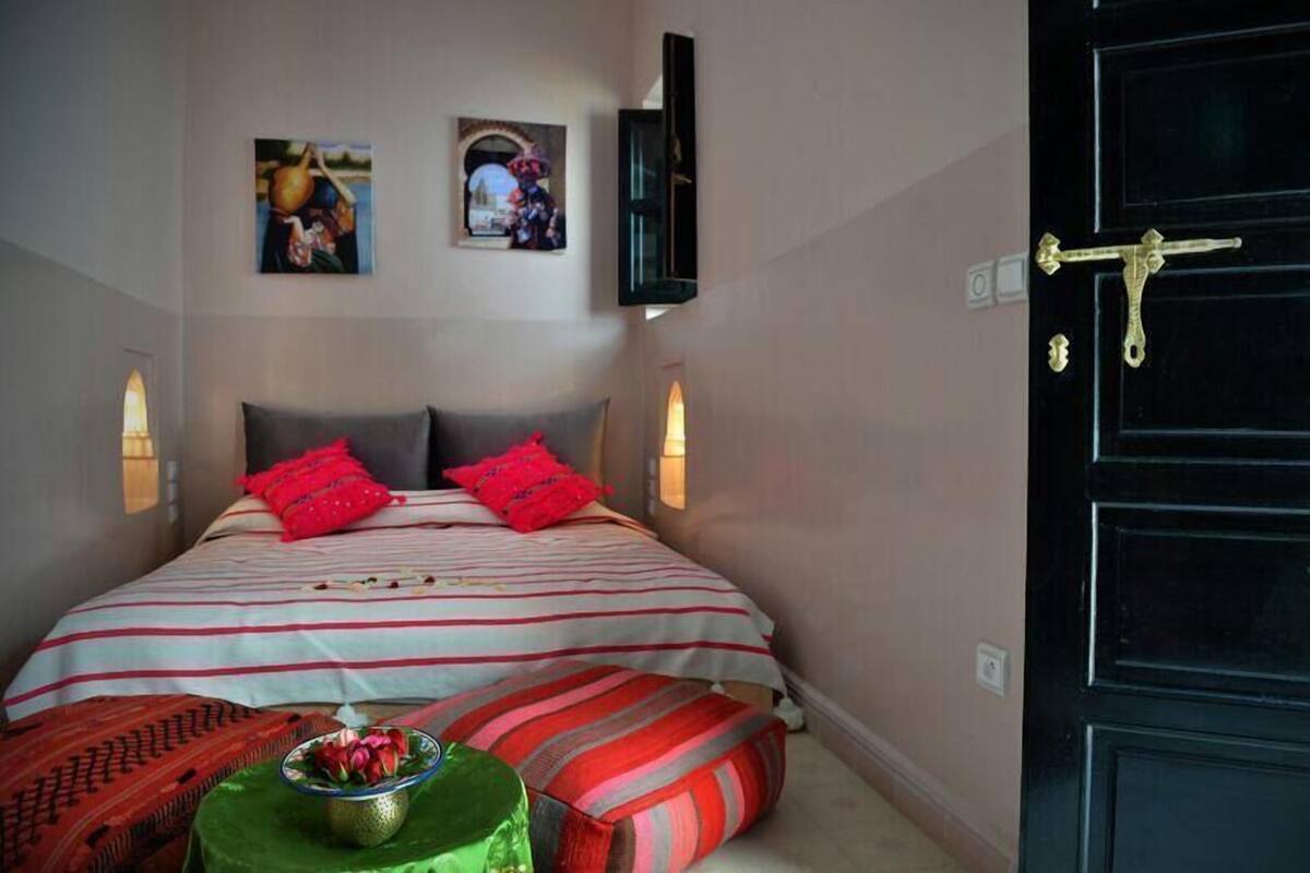 Un dormitorio con cama, almohadas, una mesita de noche con un frutero y luces en la pared.