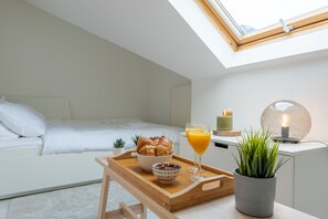 A modern bedroom with a skylight, a breakfast tray with croissants, a glass of orange juice, and a potted plant. - Jette Duplex Expo (Brussels)
