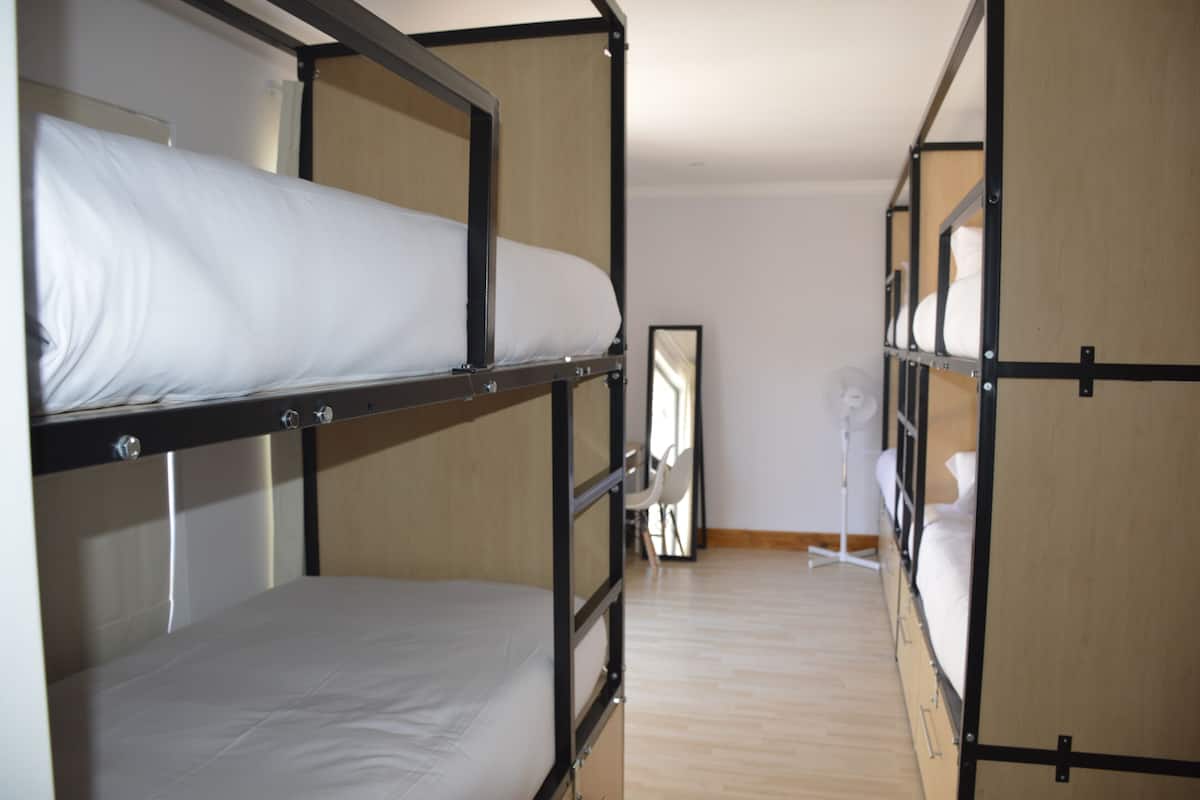 Une chambre avec des lits superposés, un plancher en bois et un miroir au mur.