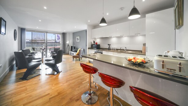 Une cuisine moderne dotée d’un îlot central, de tabourets de bar et d’un coin repas avec une table et des chaises en verre.