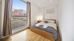 Une chambre moderne avec une grande fenêtre, un plancher en bois, un lit bien fait et deux tables de chevet.