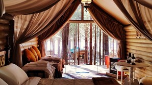 A cozy bedroom with a large bed, a small table, and a view of the forest.