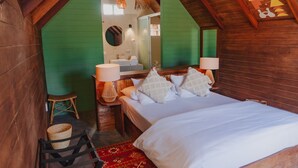 A cozy room with a wooden ceiling, a bed with white linens, two bedside lamps, a small wicker chair, and a red patterned rug. - qema Mancora (Máncora)