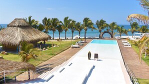 A pool area with a thatched-roof structure, palm trees, and a view of the beach. - qema Mancora (Máncora)