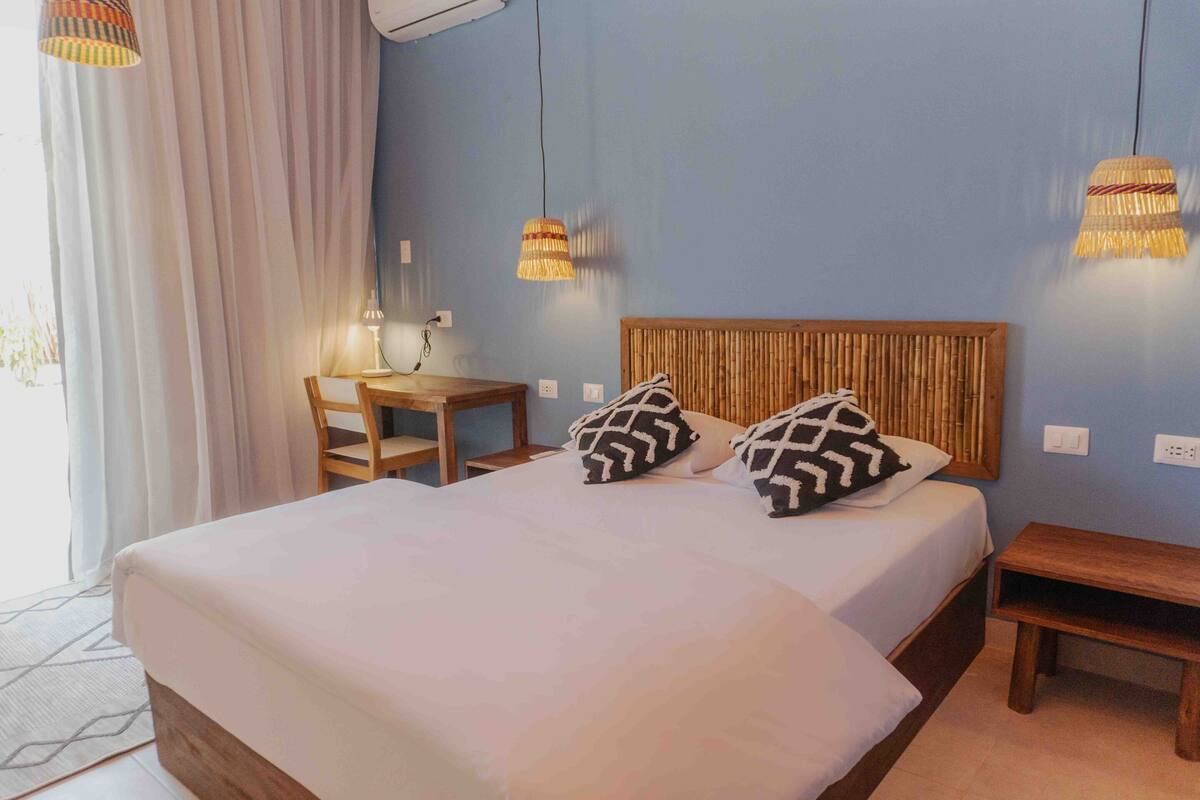 A neatly made bed with a wooden headboard, two patterned pillows, and a bedside table with a lamp.