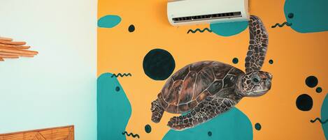 A bedroom with two beds, a wall mural of a turtle, and an air conditioning unit.
