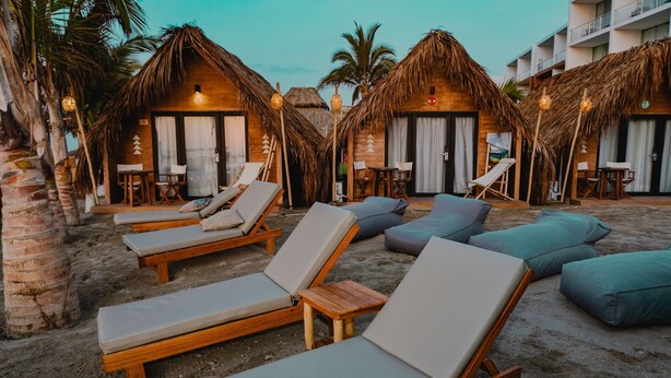 A beachside resort with wooden lounge chairs and thatched-roof huts. - qema Mancora (Máncora)