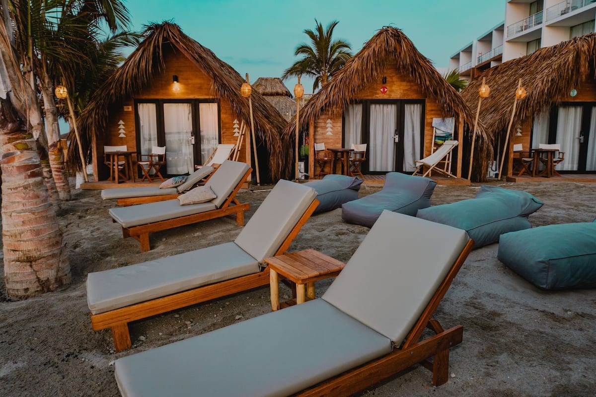 A beachside resort with wooden lounge chairs and thatched-roof huts.
