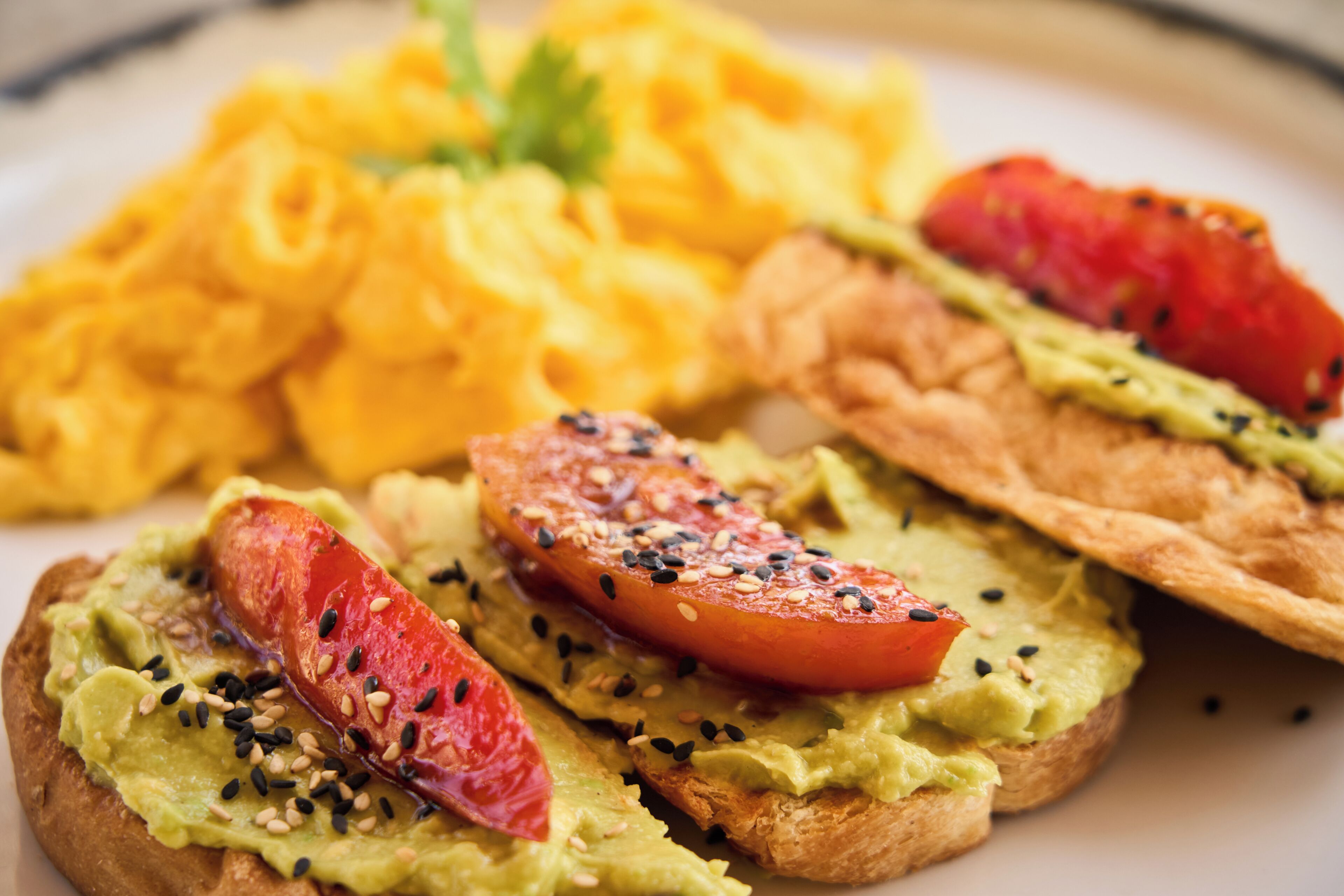 A plate with avocado toast, tomato slices, and scrambled eggs.