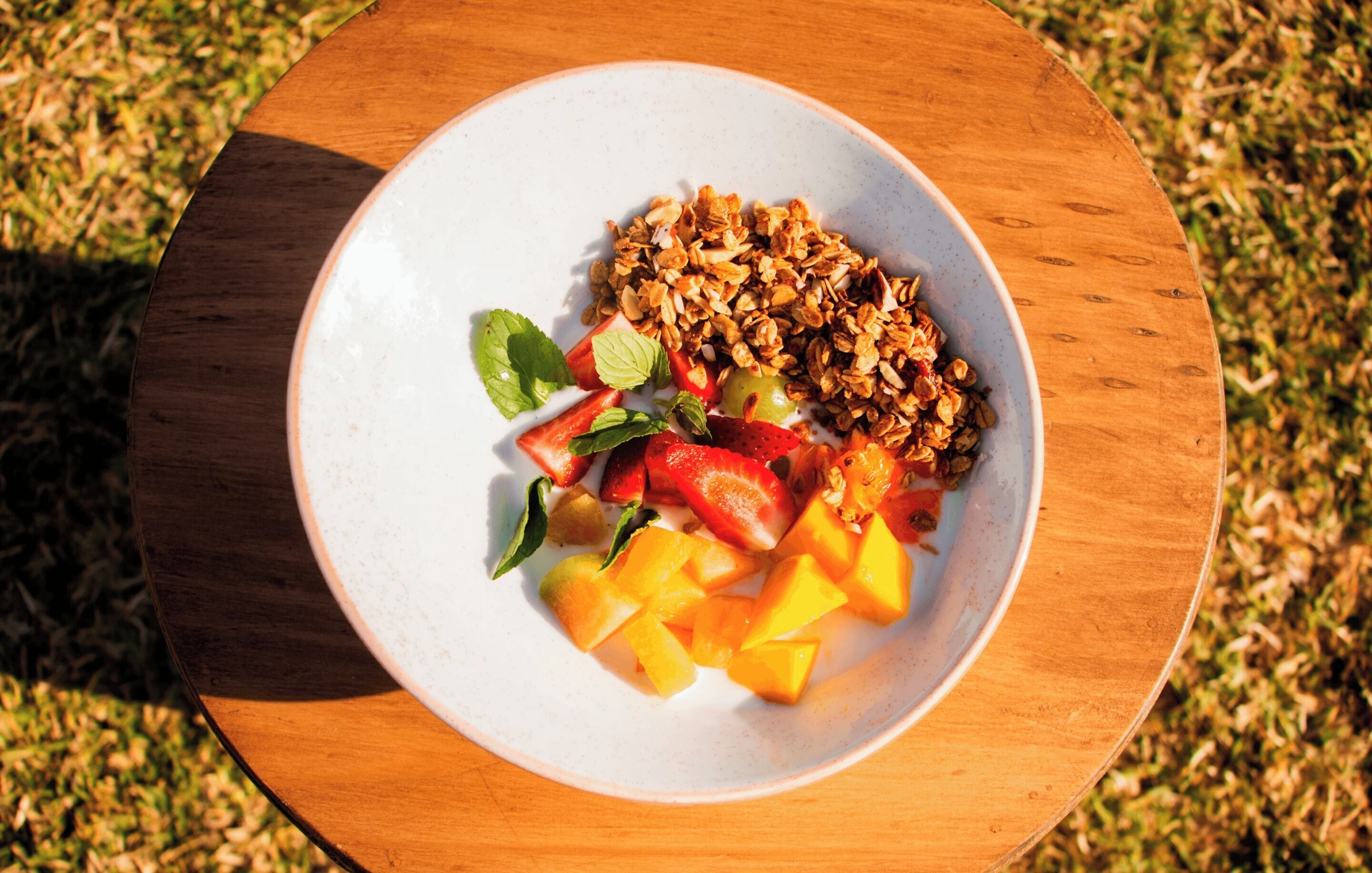A bowl of fruit and granola on a wooden table.