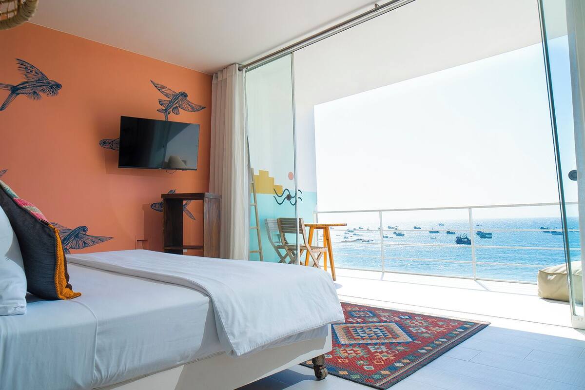 A bedroom with a bed, a TV, a window with a view of the sea, and a balcony.