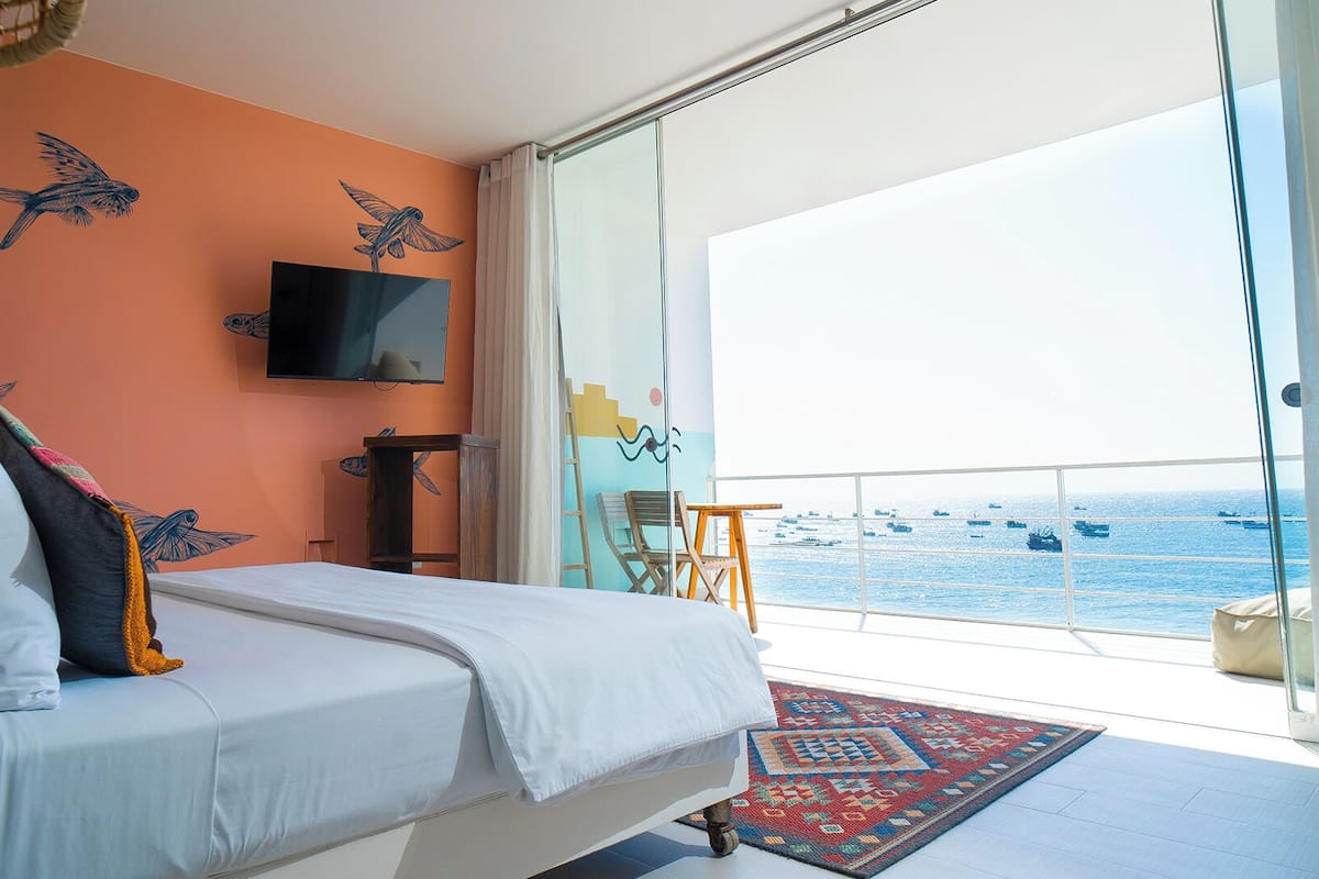 Ein Schlafzimmer mit Bett, Fernseher, einem Fenster mit Meerblick und einem Balkon.