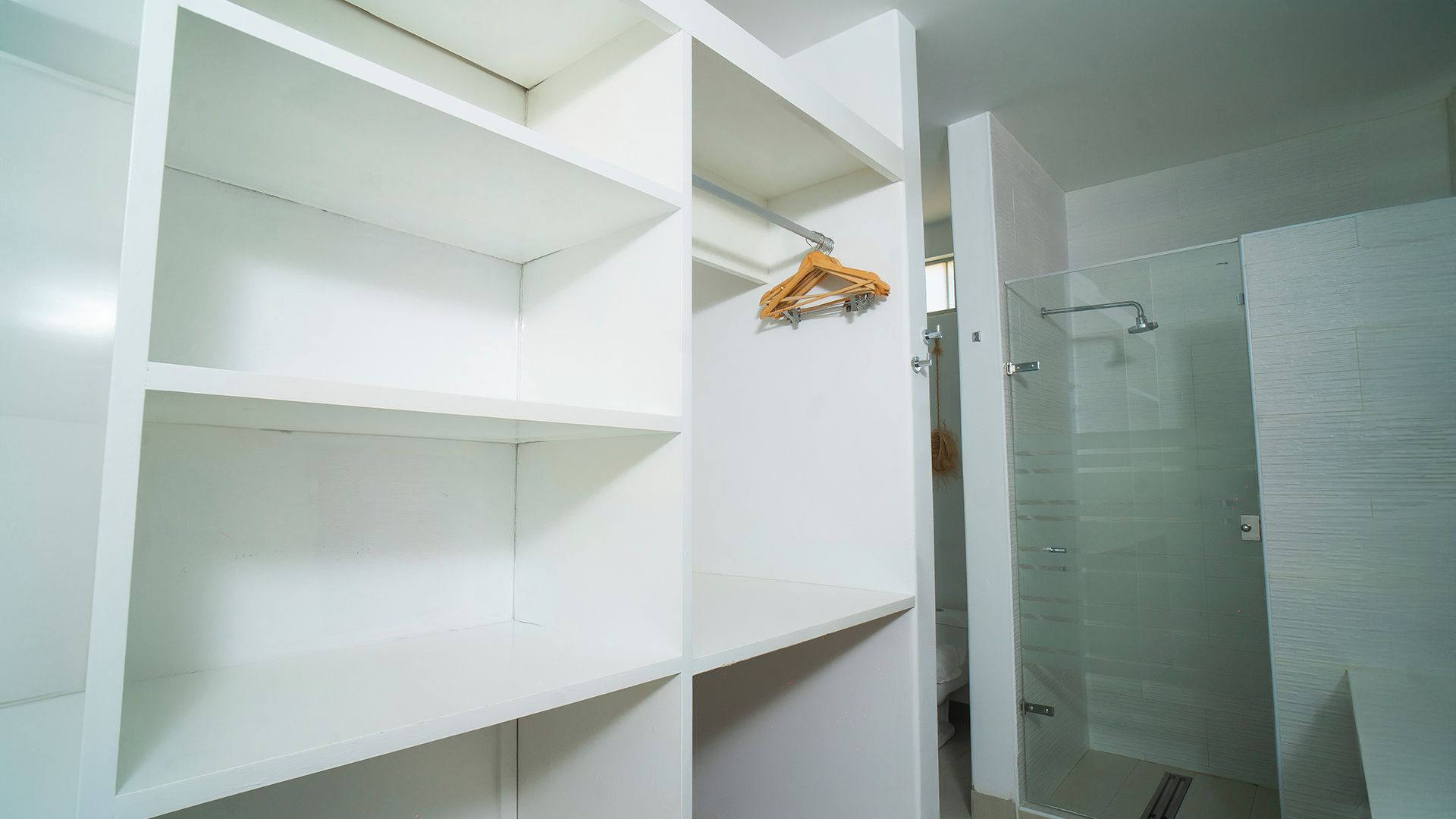 A bathroom with a glass shower enclosure, white walls, and a wooden hanger on a rack.