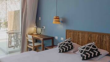 Un dormitorio con cama, dos almohadas estampadas, cabecera de madera, una mesa con sillas y una lámpara colgante.