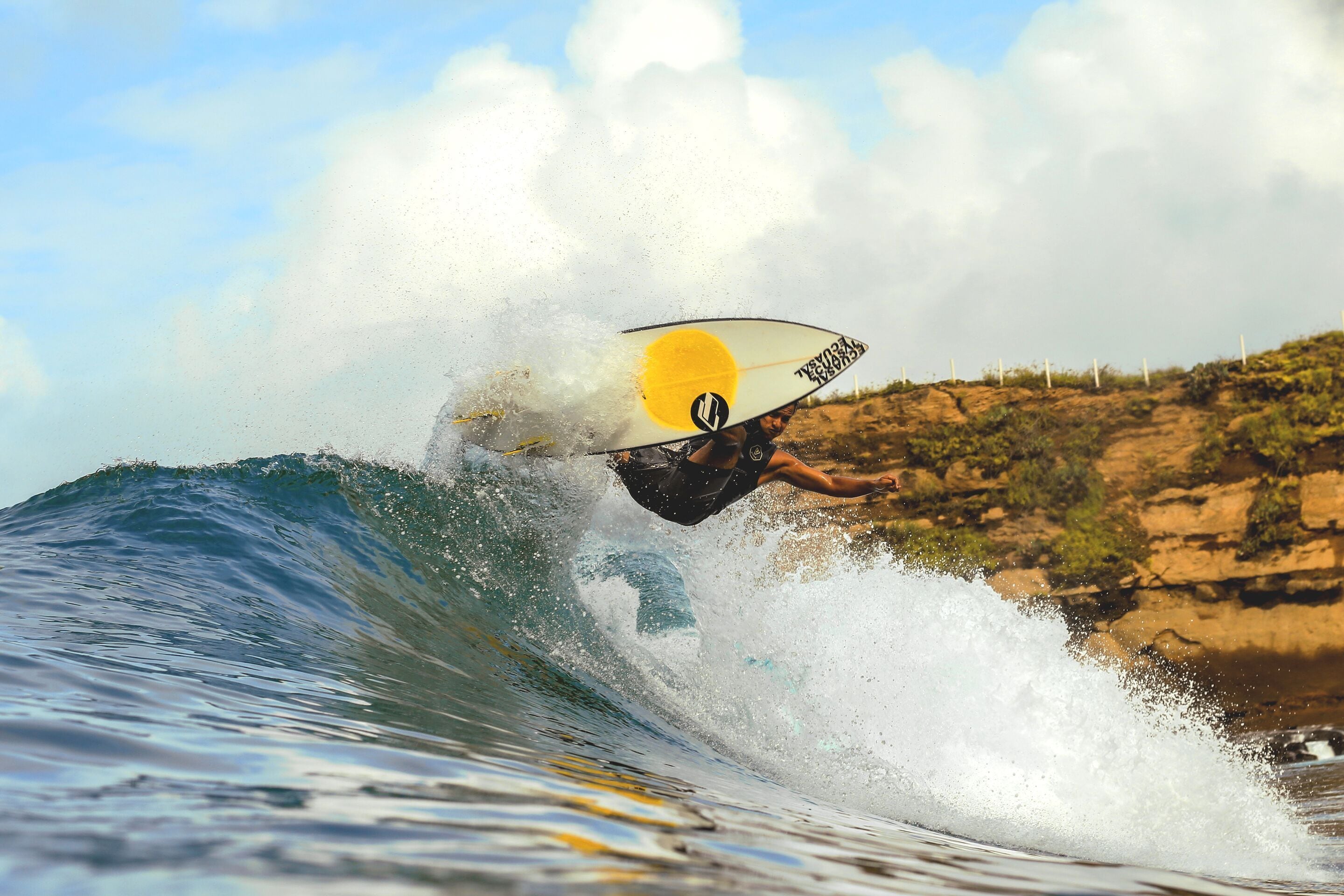 A surfer riding a wave with a surfboard that has a logo and text.