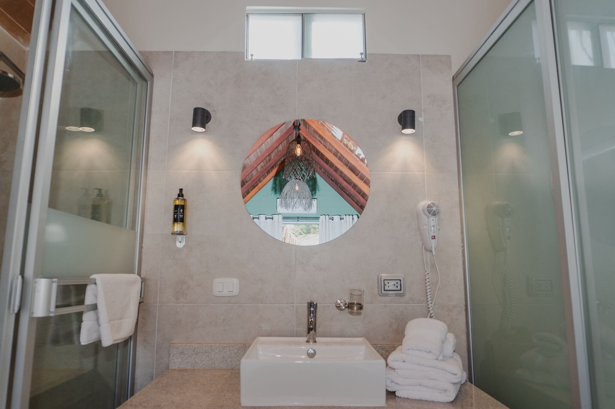 Une salle de bain moderne avec un grand lavabo, un miroir et un sèche-cheveux fixé au mur.
