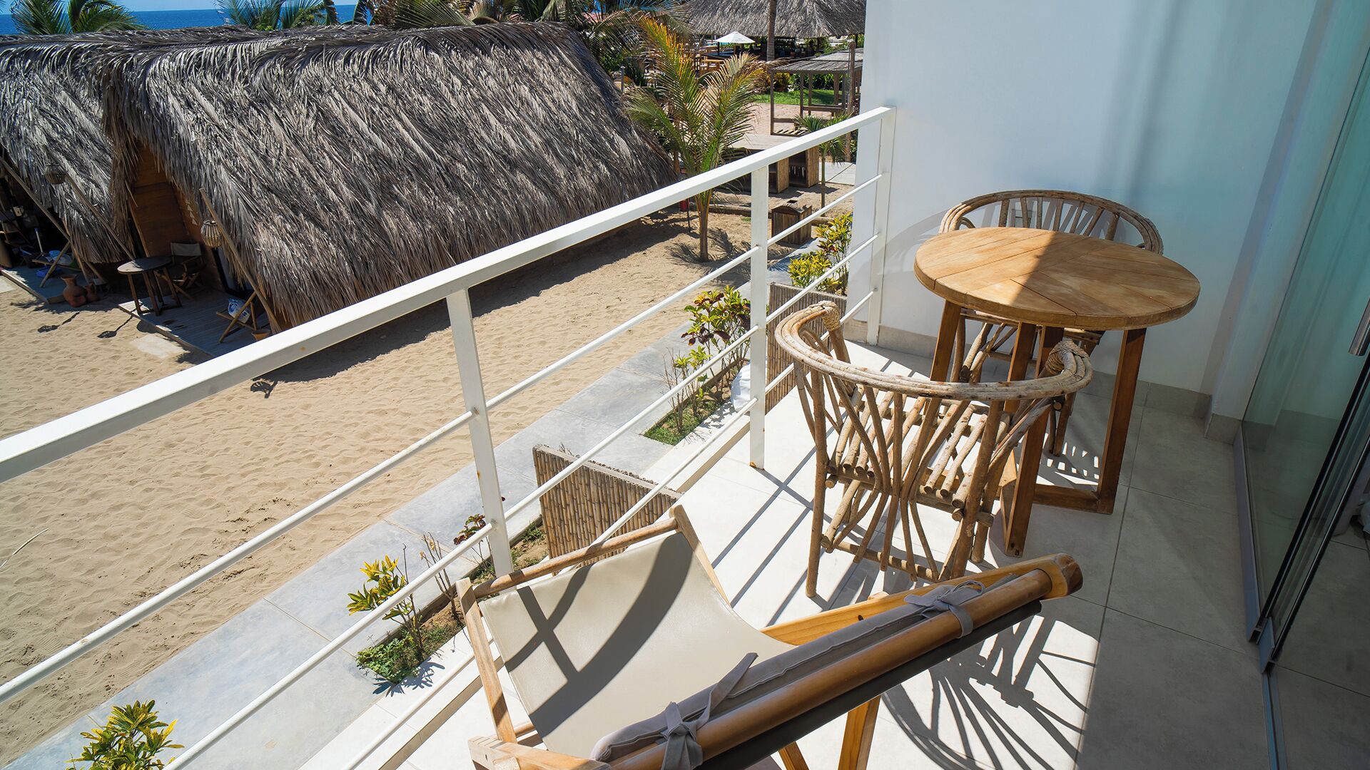 Un balcone con vista sulla spiaggia, una struttura con tetto di paglia e mobili in legno.