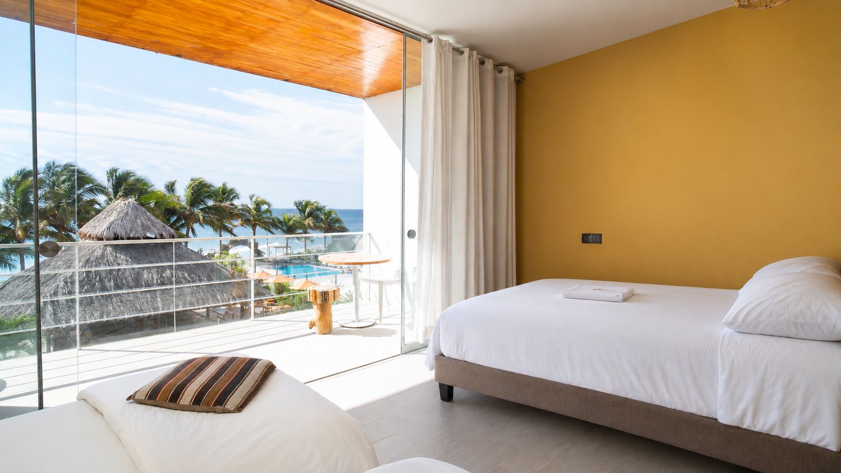 A hotel room with a bed, a view of a pool and palm trees, and a balcony with a table and chairs.
