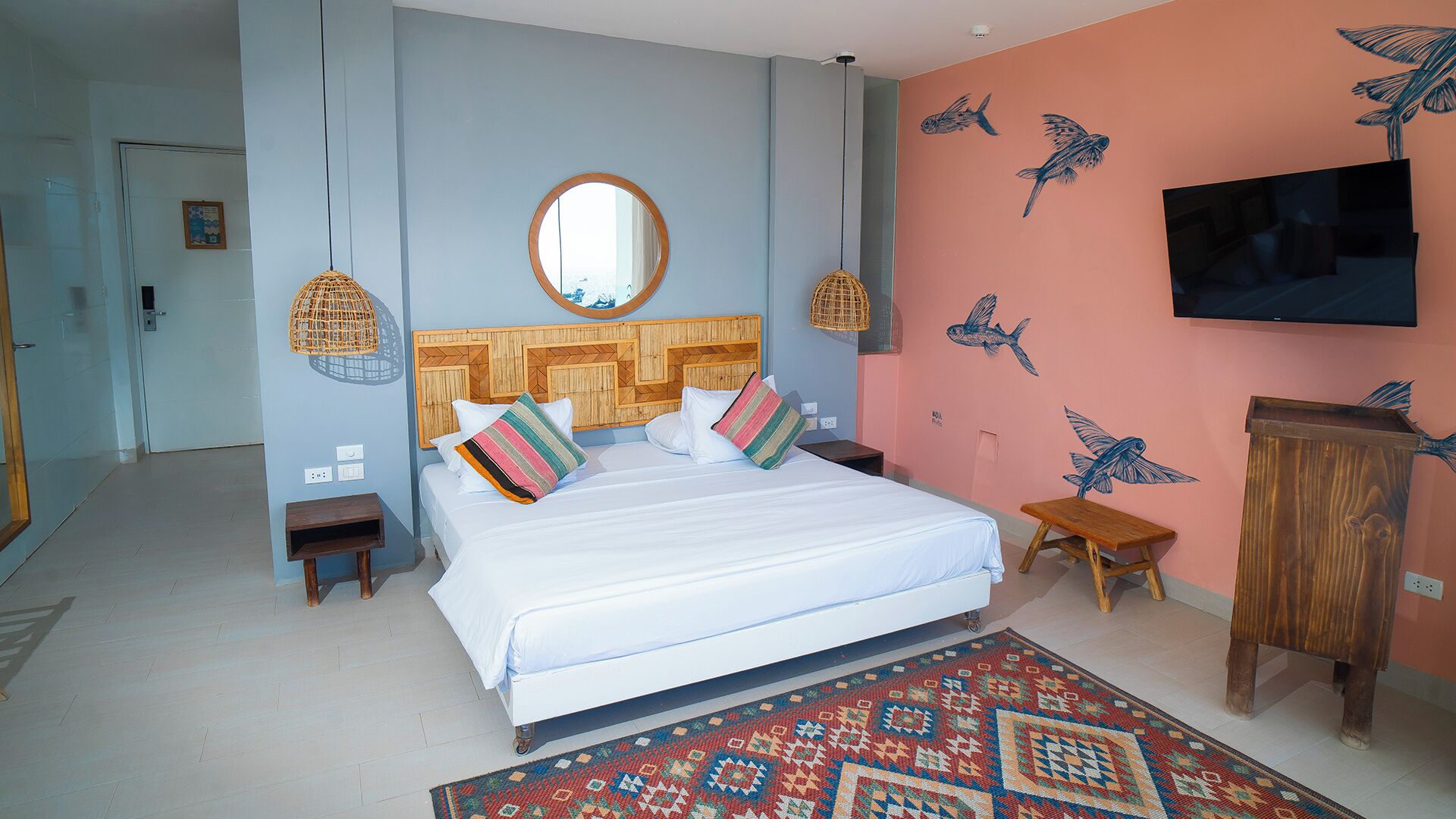 Een slaapkamer met een bed, een ronde spiegel erboven, een televisie aan de muur en een kamerkleed met dessin.