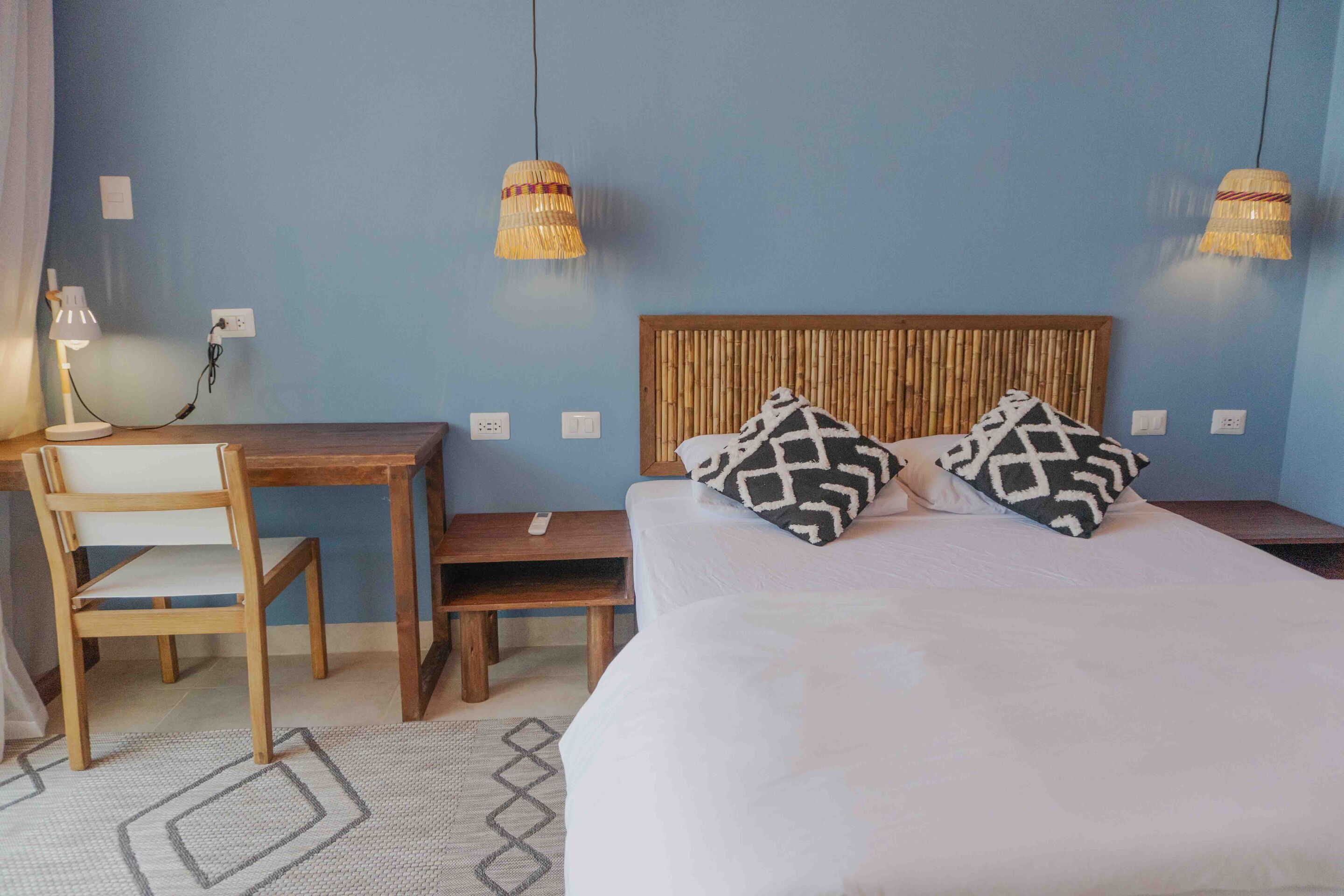 A bedroom with a bed, two bedside tables, a desk, a chair, and two wall-mounted lamps.