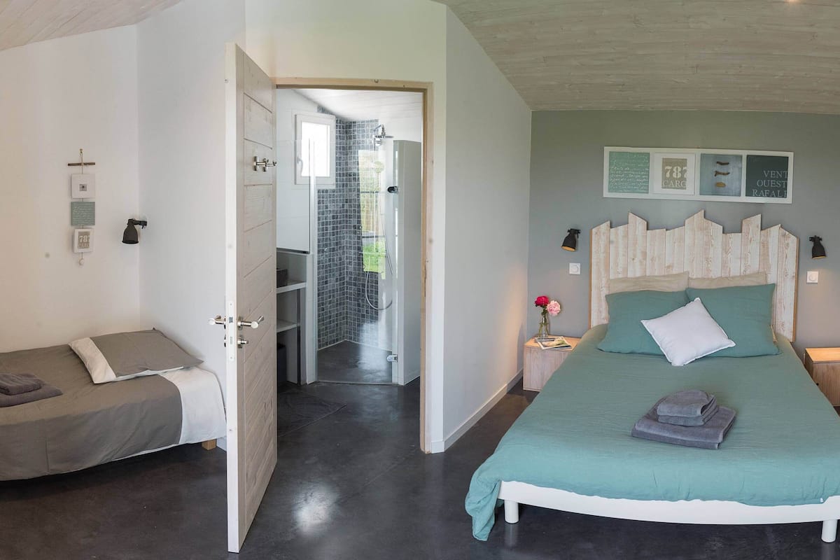 A bedroom with a bed, bedside tables, a nightstand, a shower area, and a door leading to another room.