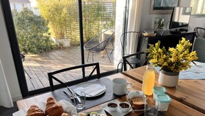 A breakfast table with croissants, fruit, and beverages, overlooking a garden with chairs and a table. - Maison d'Hotes les Petites Terres (Sainte-Marie-de-Re)