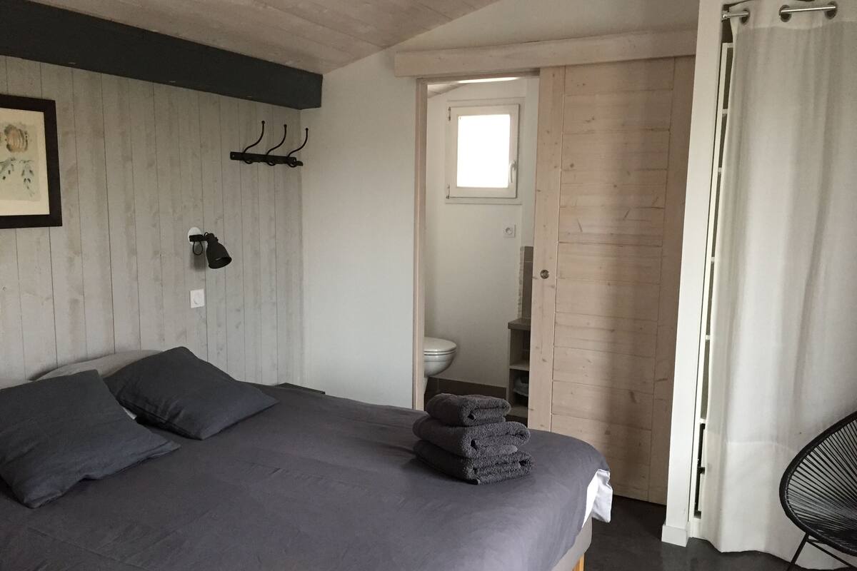 A bedroom with a bed, a small window, a door leading to a bathroom, and a chair.