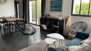 A modern living room with a dining area, featuring black wicker chairs, a blue sofa, and a wooden dining table. - Maison d'Hotes les Petites Terres (Sainte-Marie-de-Re)